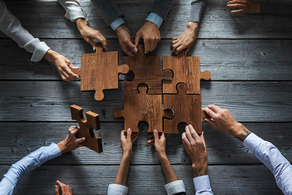 business-people-team-sitting-around-meeting-table-assembling-wooden-jigsaw-puzzle-pieces-unity-cooperation-ideas-concept 1